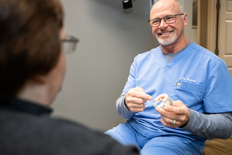 doctor smiling and and showing off dental implant model